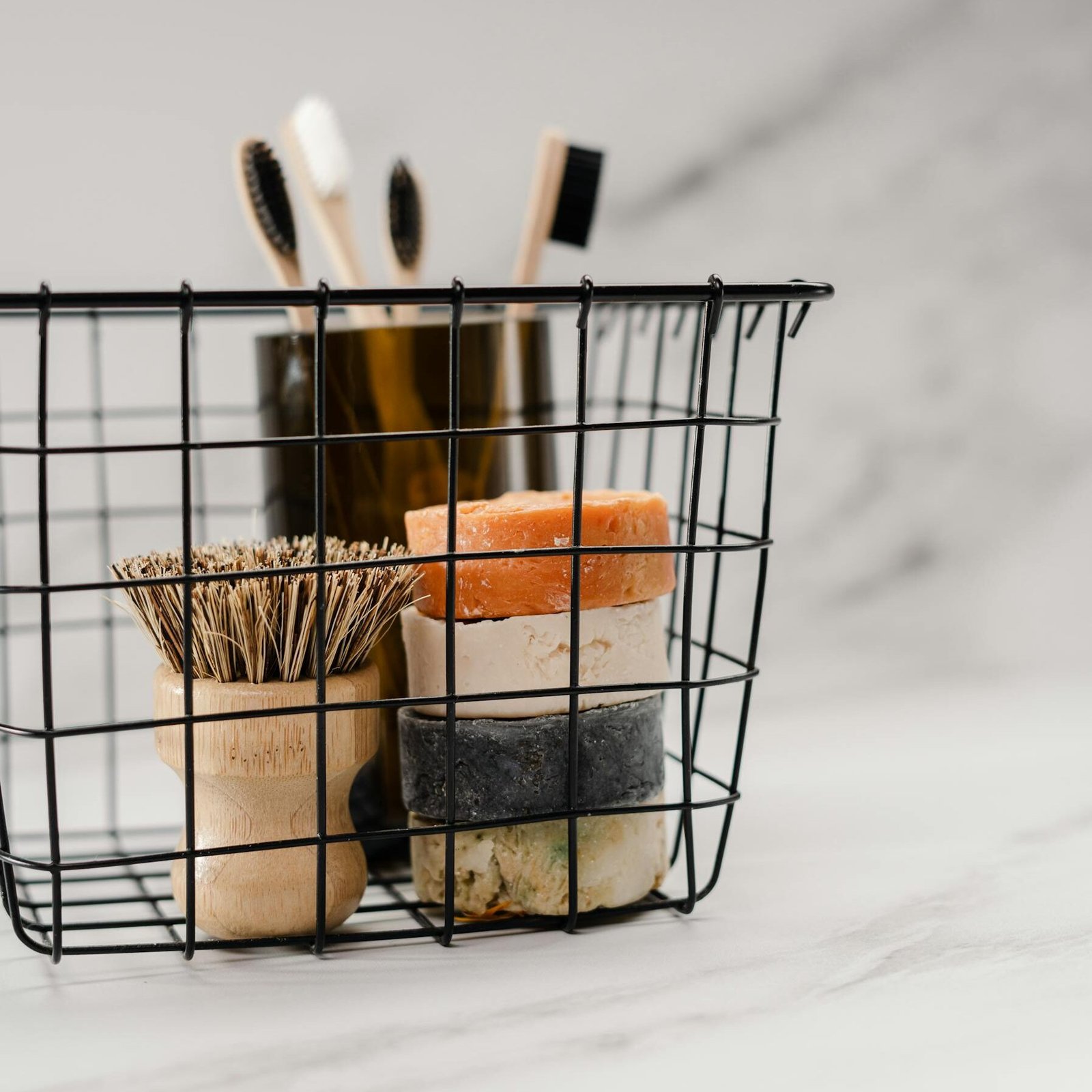 A collection of eco-friendly hygiene products including natural soaps and bamboo toothbrushes in a wire basket.